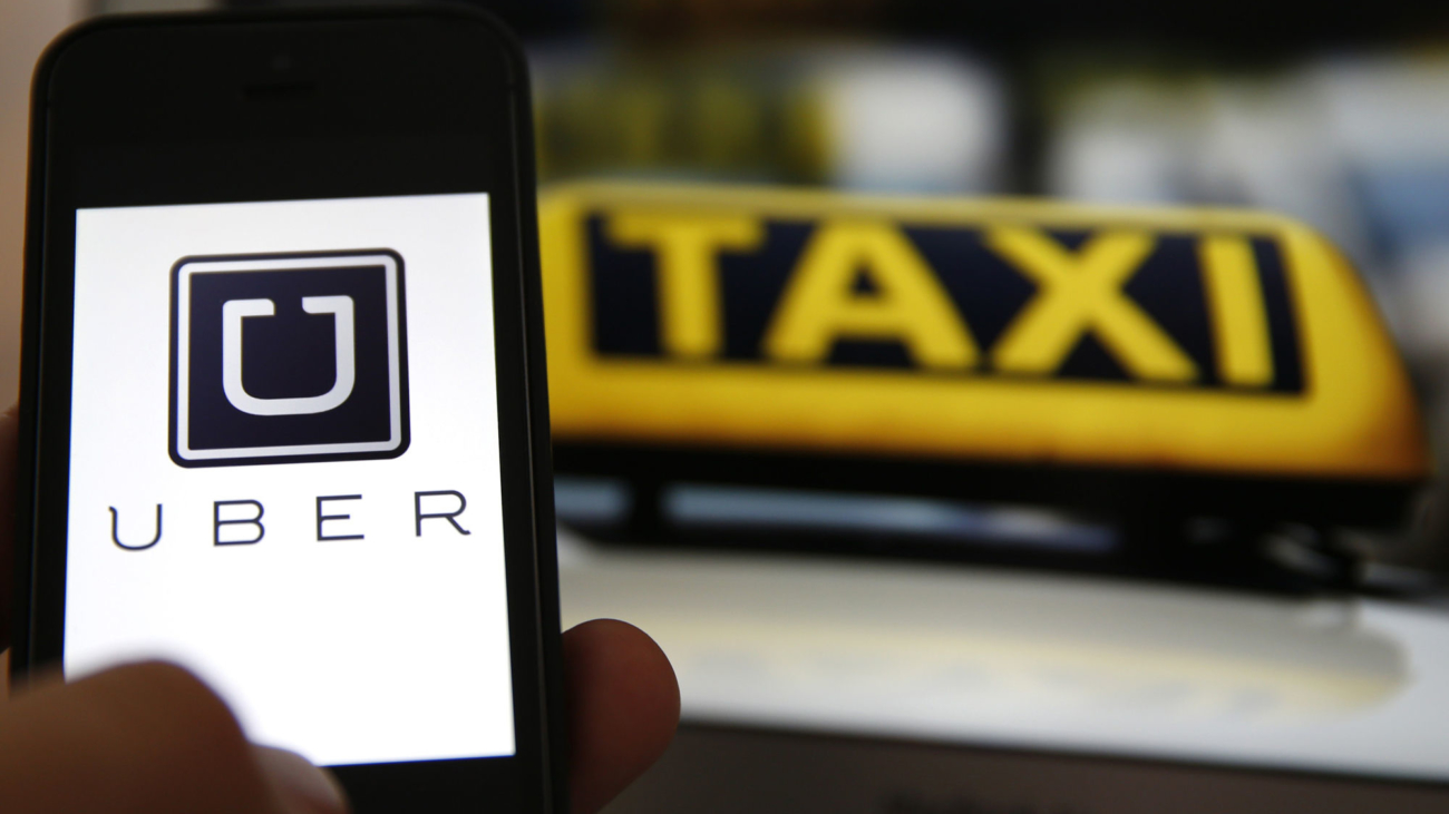 File illustration picture showing the logo of car-sharing service app Uber on a smartphone next to the picture of an official German taxi sign in Frankfurt, September 15, 2014. A Frankfurt court earlier this month instituted a temporary injunction against Uber from offering car-sharing services across Germany. San Francisco-based Uber, which allows users to summon taxi-like services on their smartphones, offers two main services, Uber, its classic low-cost, limousine pick-up service, and Uberpop, a newer ride-sharing service, which connects private drivers to passengers - an established practice in Germany that nonetheless operates in a legal grey area of rules governing commercial transportation.    REUTERS/Kai Pfaffenbach/Files  (GERMANY - Tags: BUSINESS EMPLOYMENT CRIME LAW TRANSPORT)